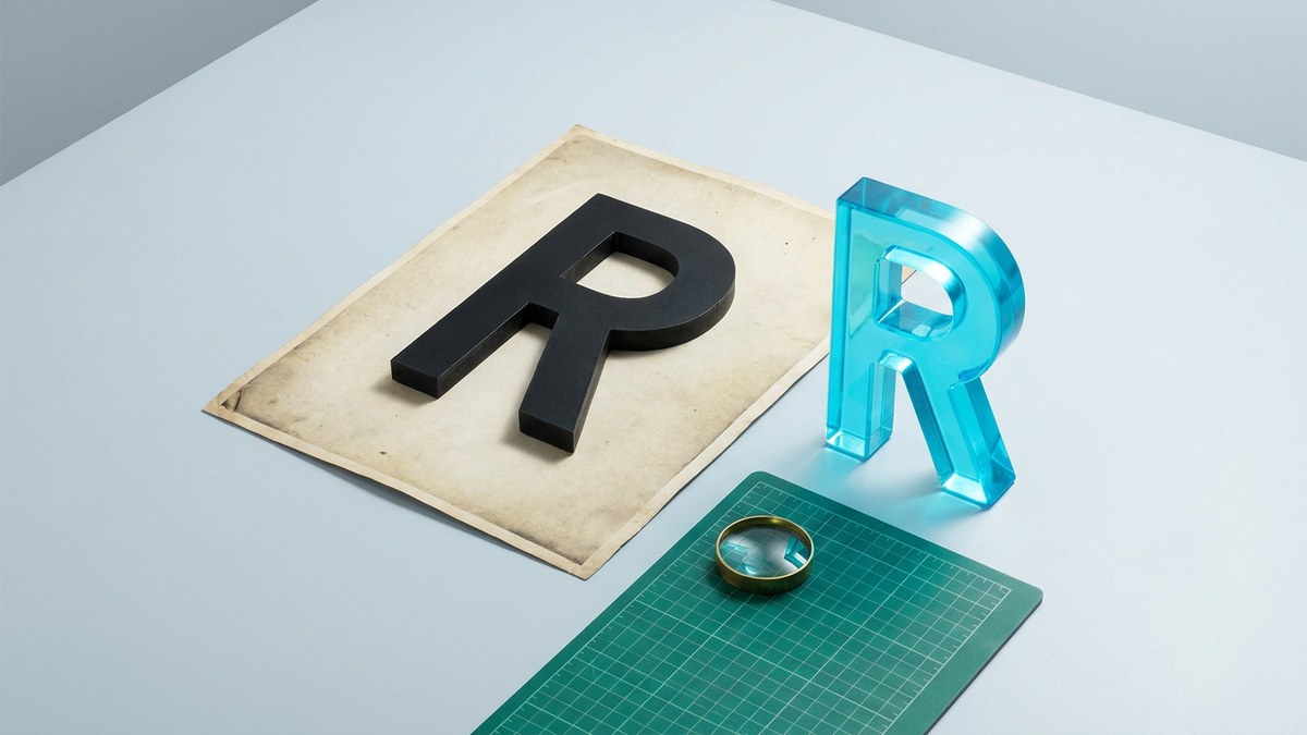 A black R specimen and cyan glass R beside a magnifying lens on a design desk